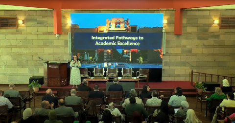 Professor Hoda Mostafa is standing on stage with a big screen behind her displaying the text: Integrated Pathways for Academic Excellence
